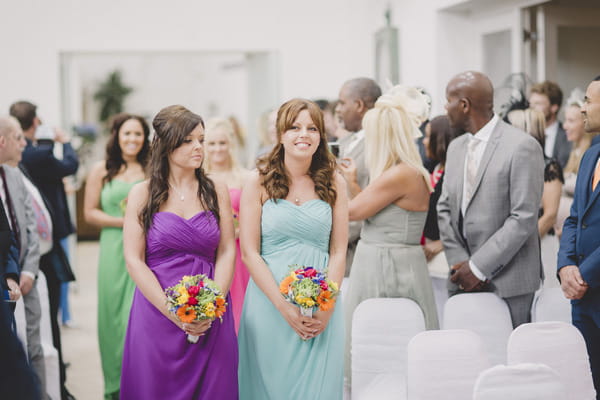 Bridesmaids walking down aisle in bright dresses