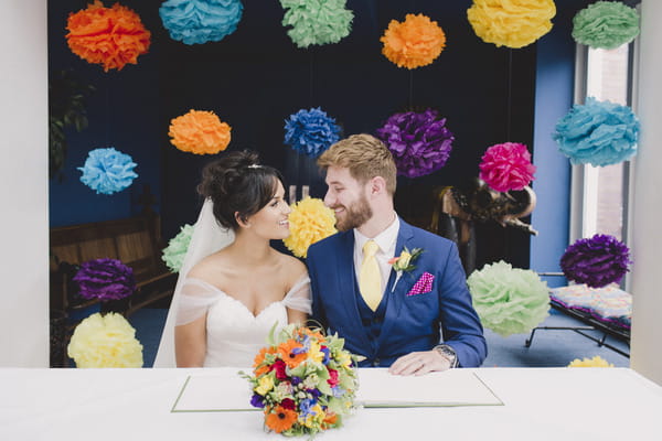 Bride and groom sign register in front of colourful backdrop