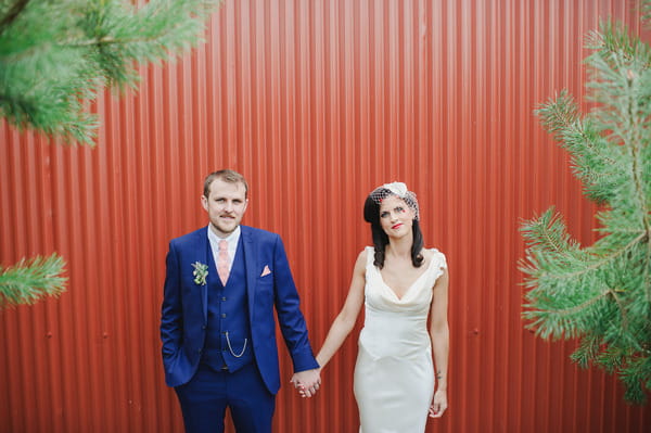 Bride and groom holding hands in front of red metal wall