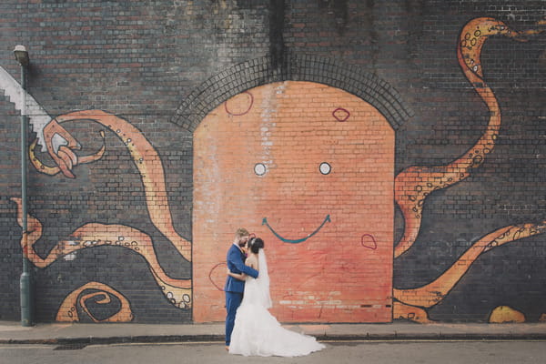 Bride and groom standing in front of wall with octopus graffiti