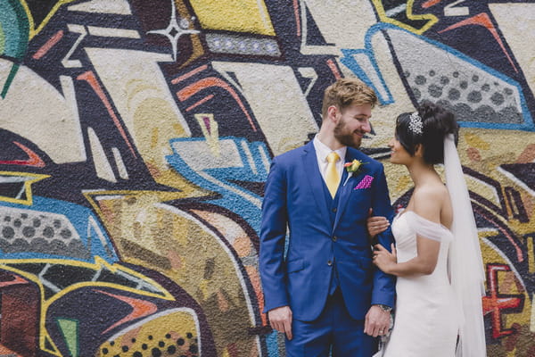 Bride and groom in front of graffiti covered wall