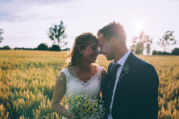 Bride and groom touching heads in field