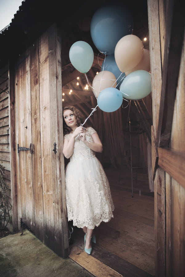 Bride at entrance to barn holding balloons