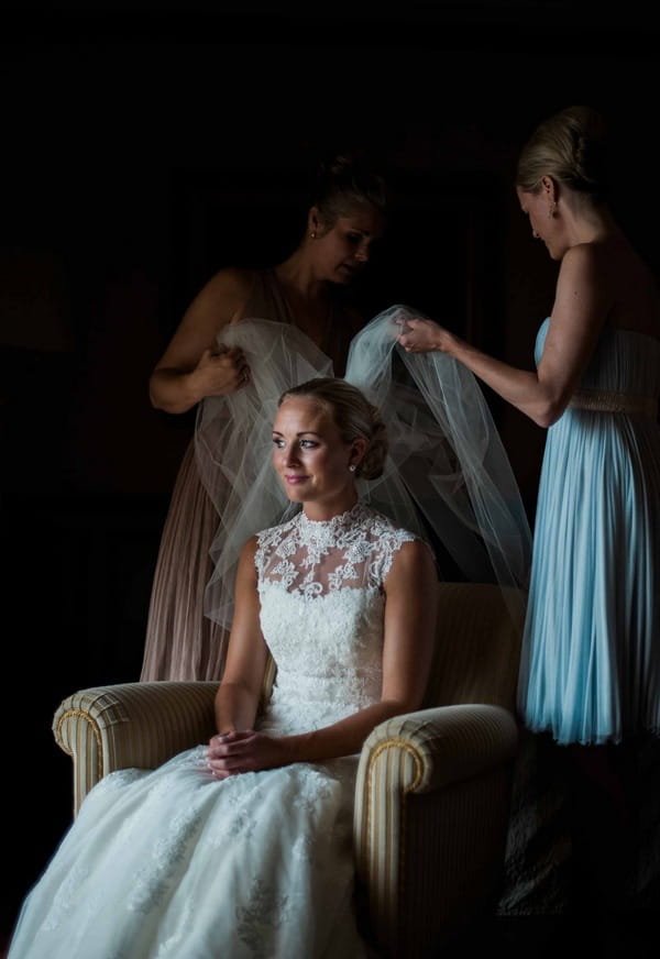 Bride sitting in chair putting veil on