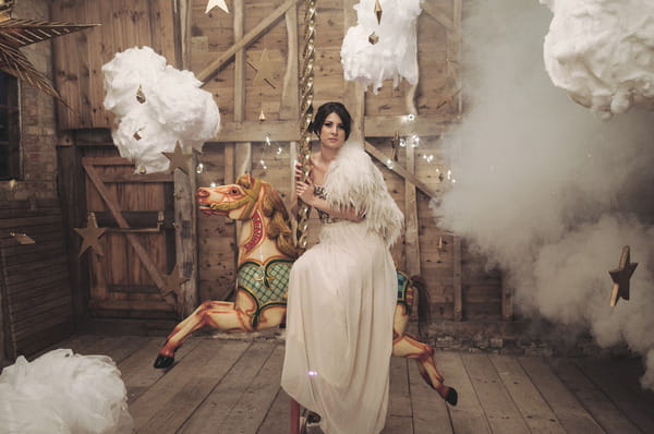 Bride sitting on carousel horse surrounded by clouds