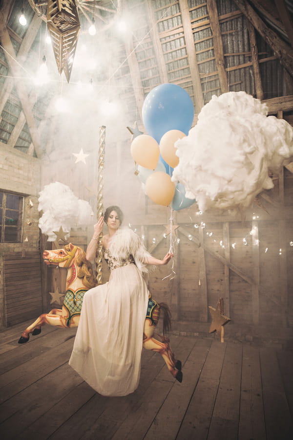 Bride sitting on carousel horse surrounded by clouds