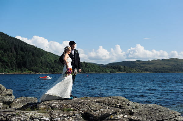 Bride and groom standing on rocks overlooking Loch Melfort