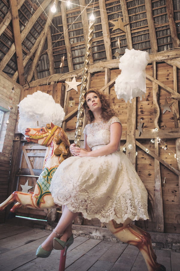 Bride sitting on carousel horse with clouds hanging down