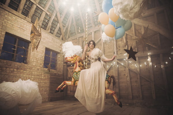 Bride sitting on carousel horse with clouds hanging down