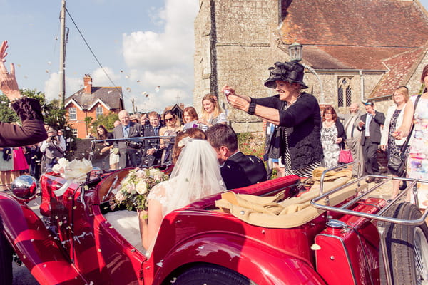 Lady throwing confetti over bride and groom in vintage MG TC 1947 wedding car