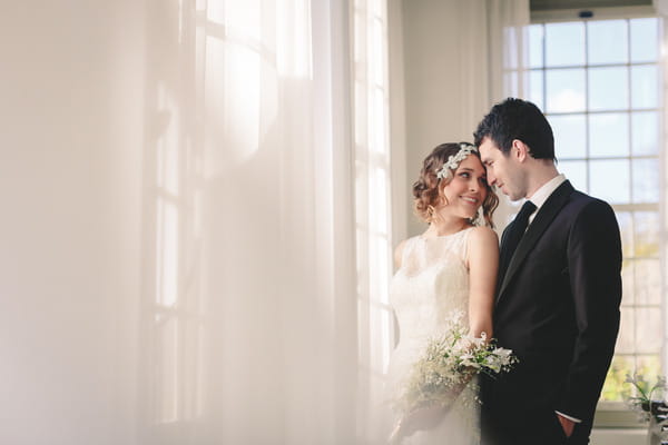 Bride and groom standing by window