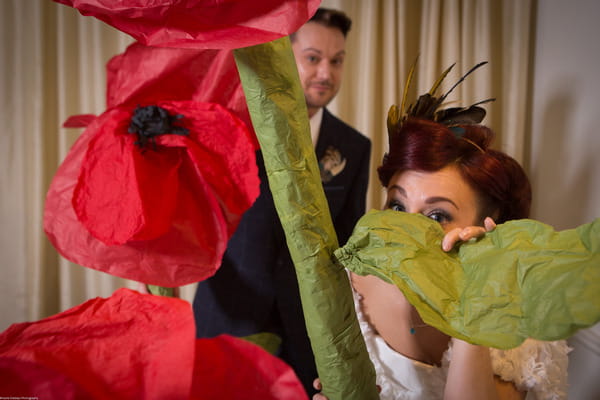 Bride and groom peering through large paper poppies