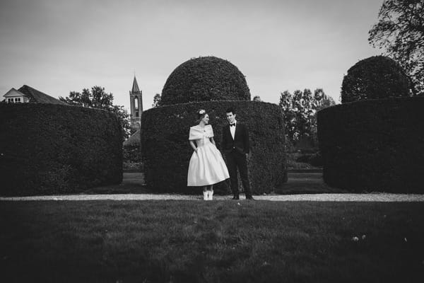 Bride and groom standing up against hedge