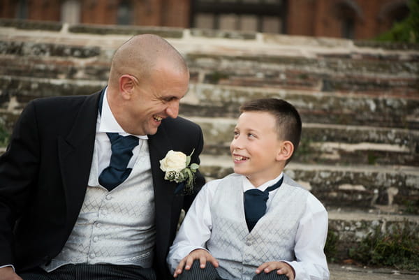 Groom sitting on steps of Layer Marney Tower with pageboy