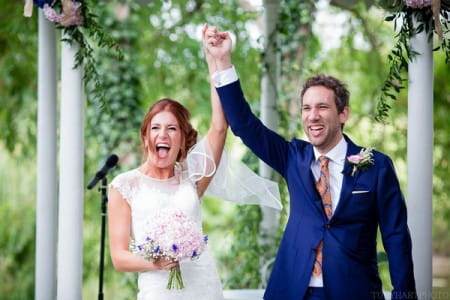 Happy bride and groom holding hands in the air - Picture by Tony Hart Photography