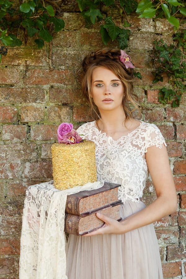 Bride holding wedding cake standing next to wall