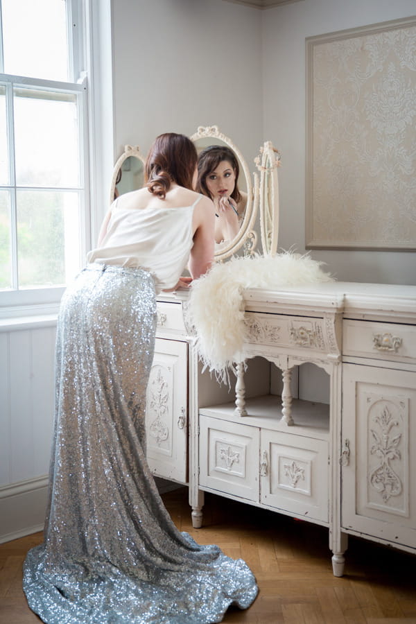 Bride in glittery silver skirt doing make-up in mirror