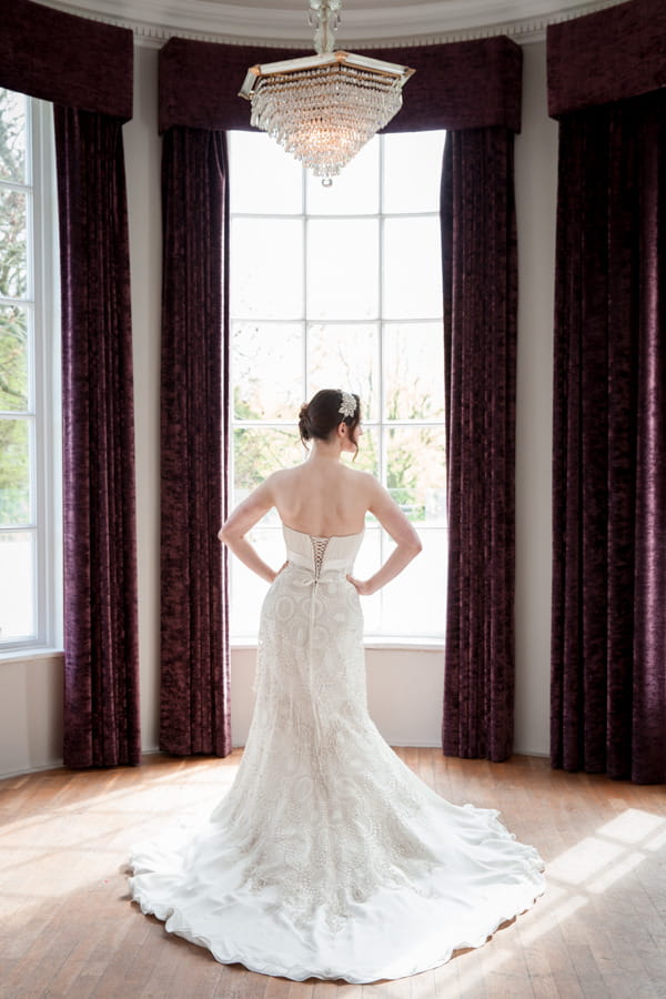 Bride with hands on hips show detail on back of wedding dress