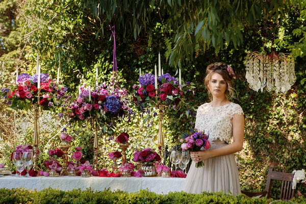 Bride holding bouquet standing next to long styled wedding table