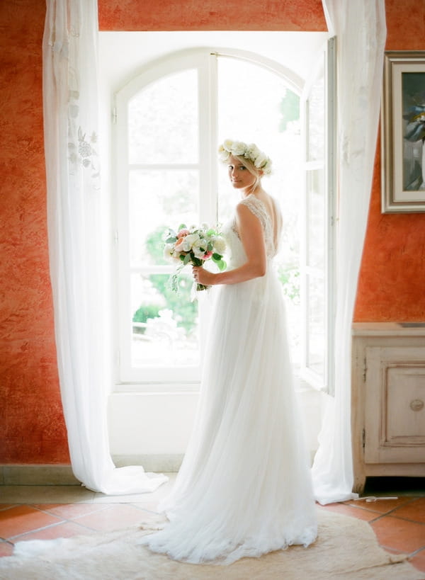 Bride with flower crown holding bouquet by window