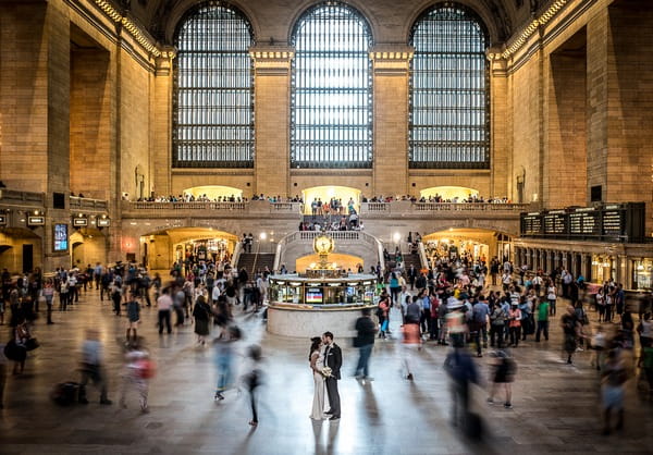 Bride and groom in train station with passengers moving around them - Picture by James Tracey Photography