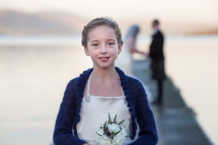 Flower girl standing on jetty with bride and groom in background - Picture by Lorraine Bhandari Photography and Videography