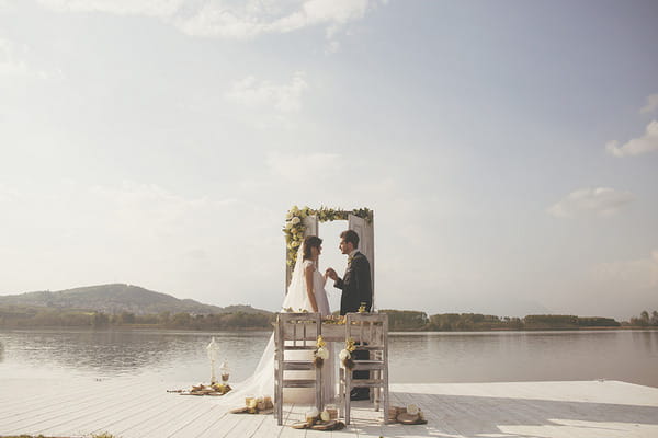 Bride and groom on jetty by Lake of Candia in Italy