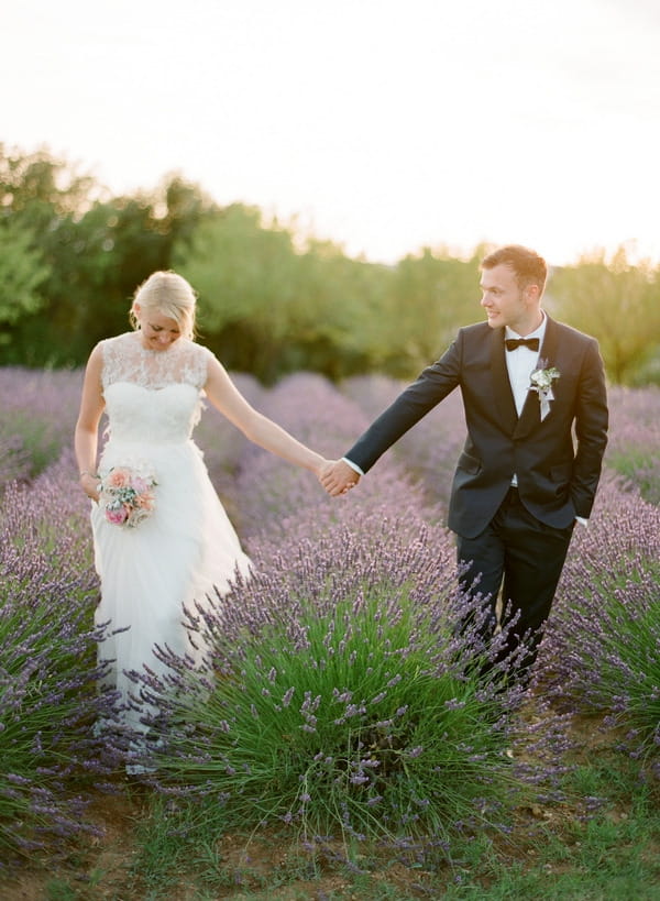 Bride and groom holding hands in field of lavender in Provence