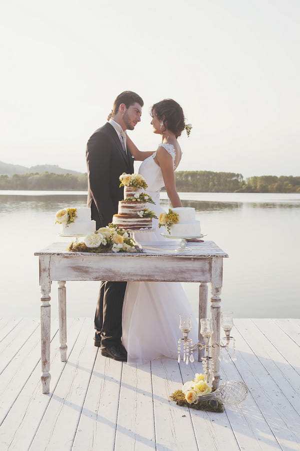 Bride and groom by wedding cake table in front of Lake of Candia in Italy