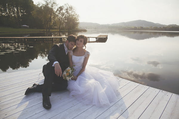 Bride and groom sitting on jetty by Lake of Candia in Italy