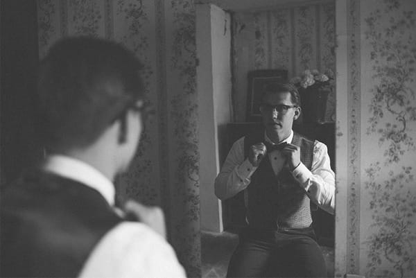 Groom adjusting bow tie in mirror