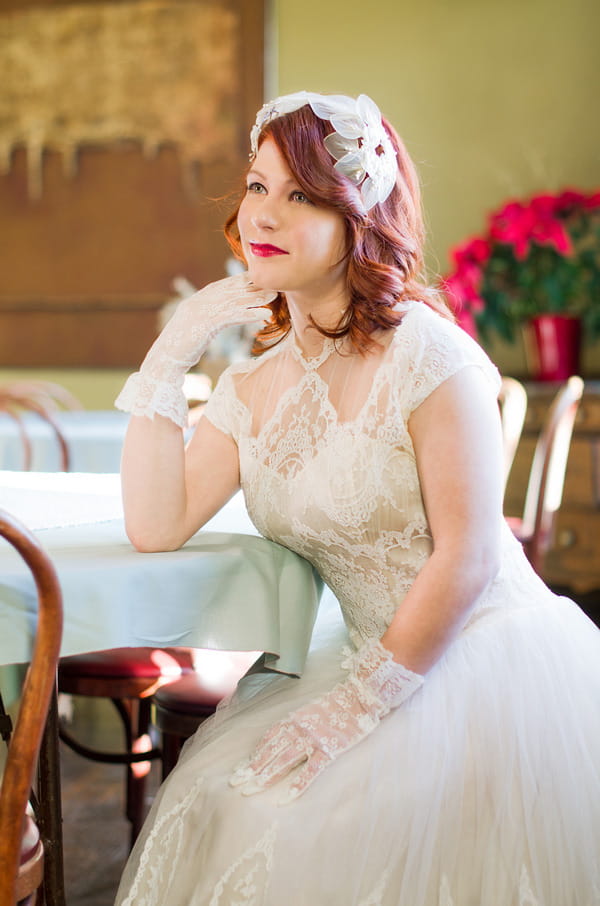 Bride wearing vintage wedding dress and gloves, leaning on table