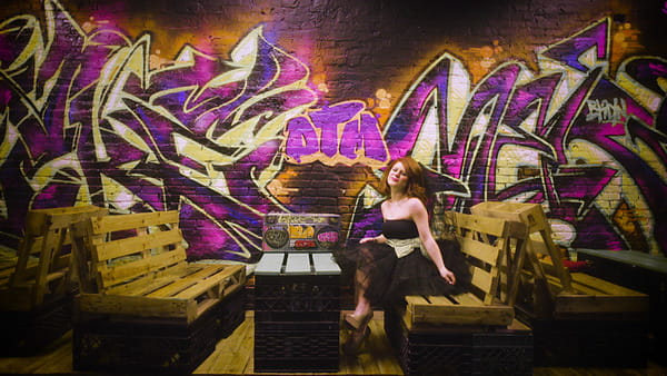 Bride in black wedding dress sitting next to graffiti wall