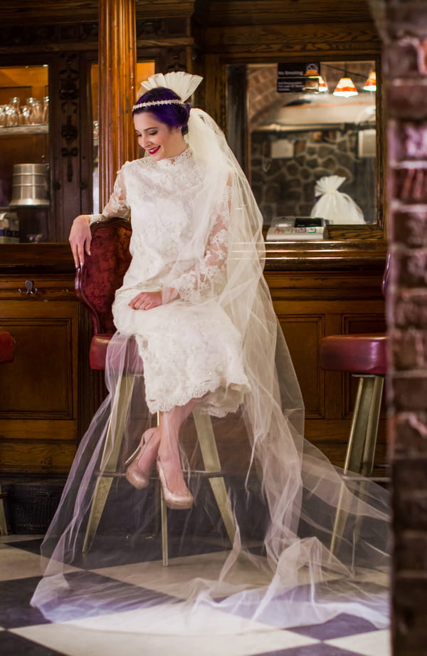 Bride wearing vintage wedding dress and long veil, sitting on bar stool