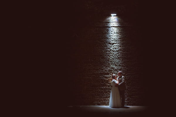Bride and groom by wall under spotlight