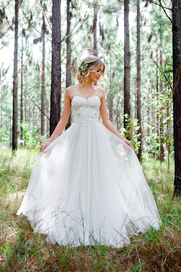 Bride standing in woodland holding out dress