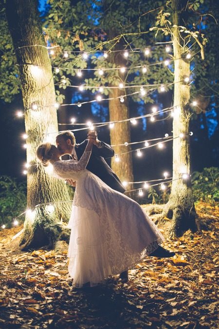 Bride and groom kissing in front of trees with strings of lights - Picture by Danielle Victoria Photography