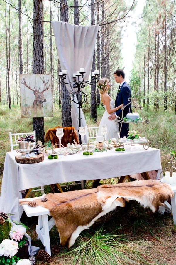 Bride and groom standing behind wedding table in woodland