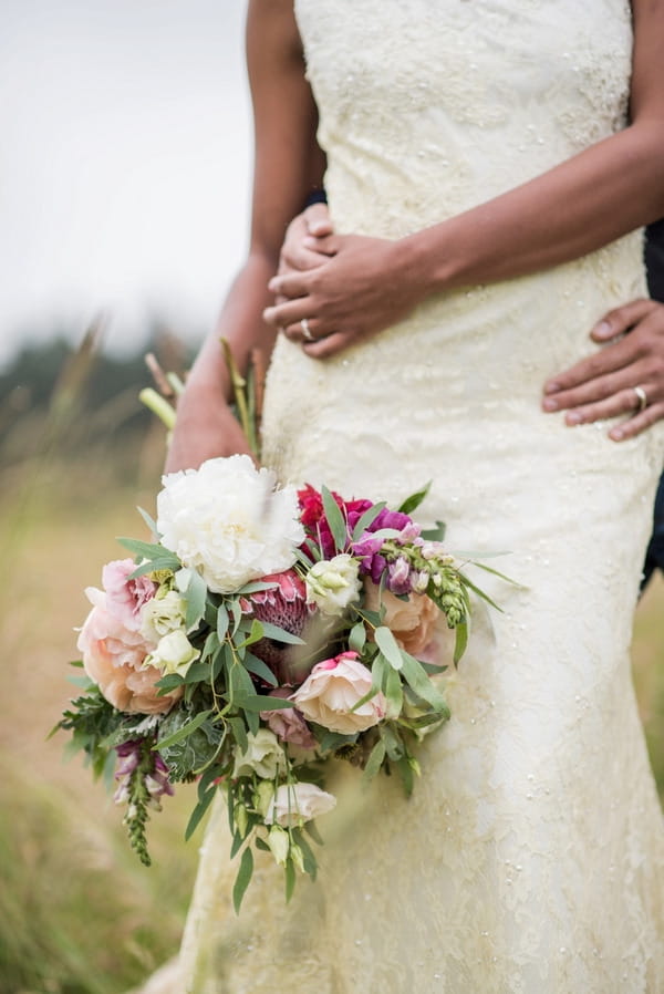 Bride's rustic wedding bouquet and groom's arm around her waist