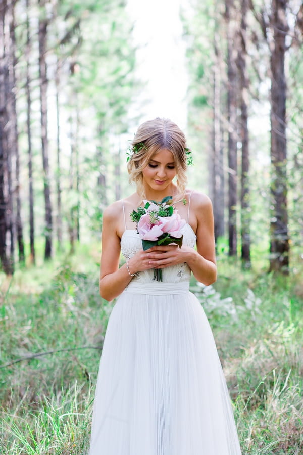 Bride looking down at bouquet in woodland