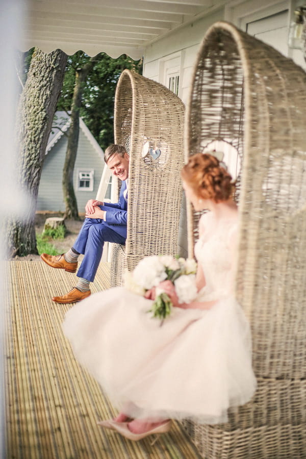 Bride and groom sitting on chairs looking at each other outside house at Woodhill Hall