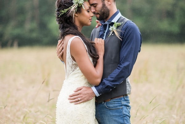 Bride and groom facing each other in meadow resting heads