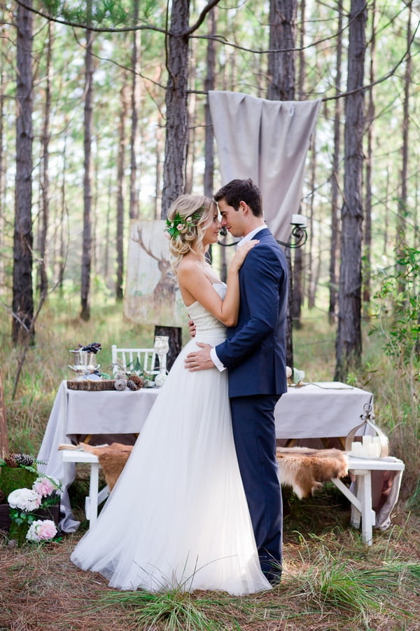 Bride and groom standing in front of wedding table in woodland