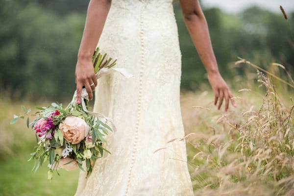 Bride walking with rustic bouquet through meadow