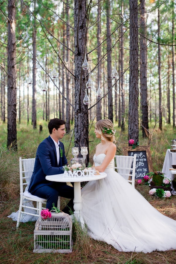 Bride and groom sitting at table in woodland