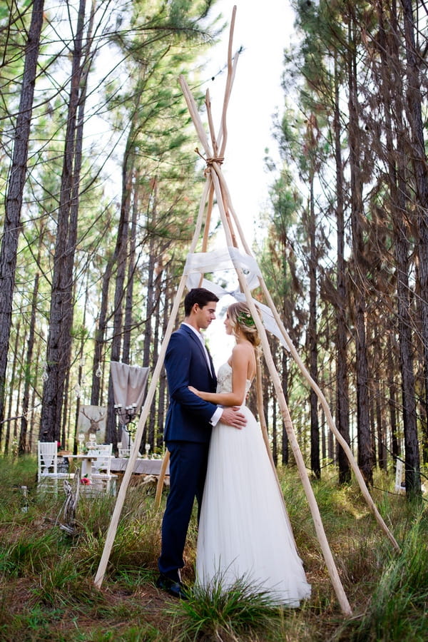 Bride and groom standing under tipi frame