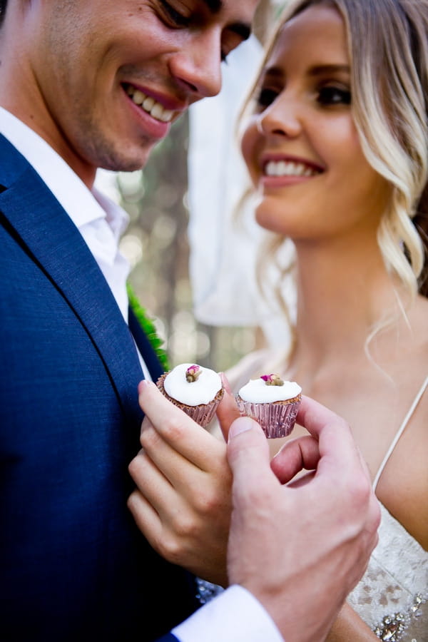 Bride and groom holding small cupcakes