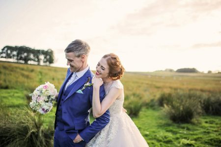 Happy bride leaning on groom in countryside