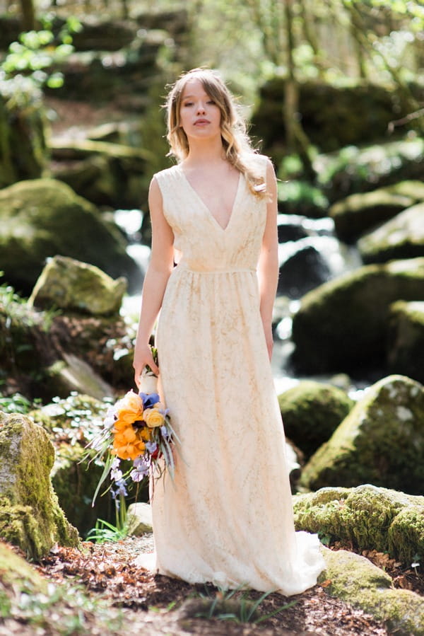 Bride holding bouquet by rocks in woods