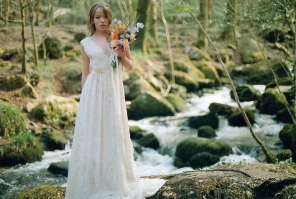 Bride holding bouquet by stream in woods